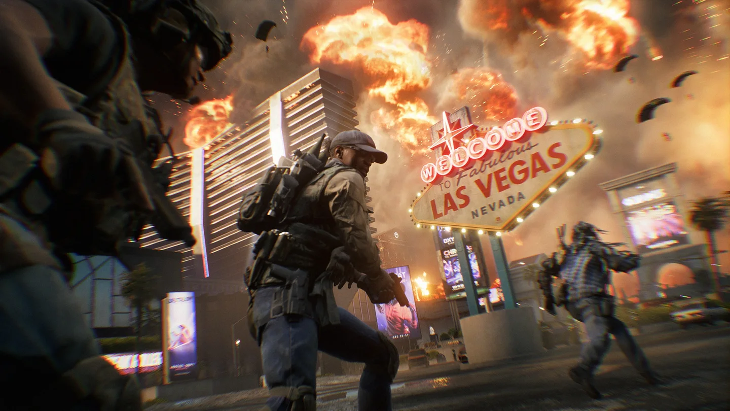 Soldiers run along a street as massive explosions erupt overhead, with parachutes descending around an illuminated “Welcome to Fabulous Las Vegas” sign.